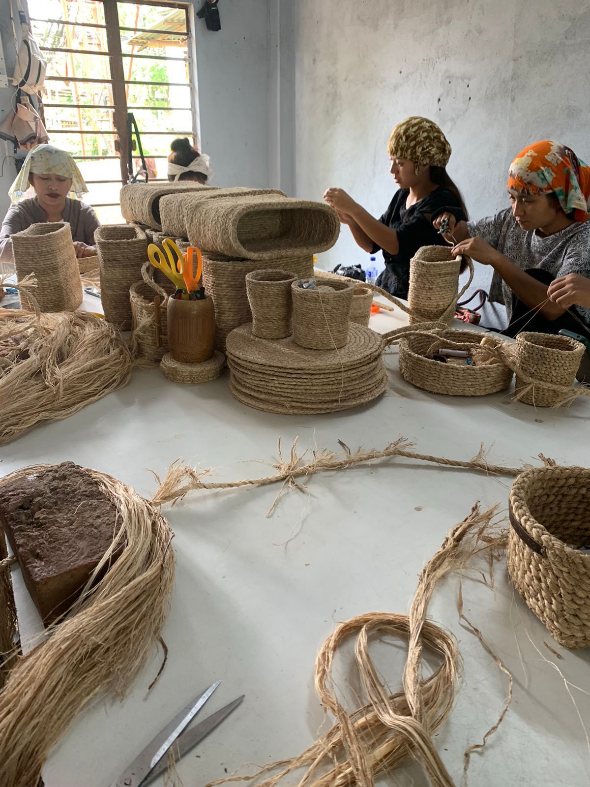 People working with woven materials on a table in a workshop setting.