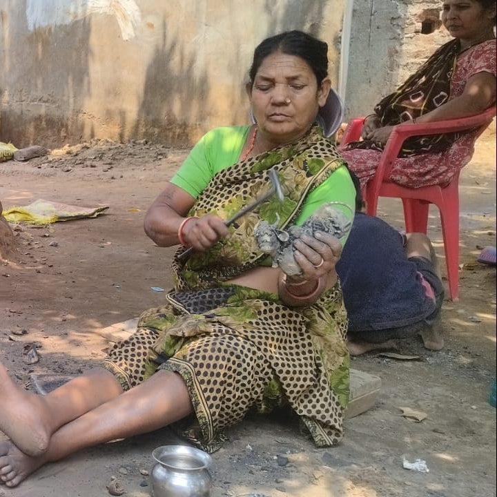 Three women sitting on the ground in a village setting, engaged in an activity.