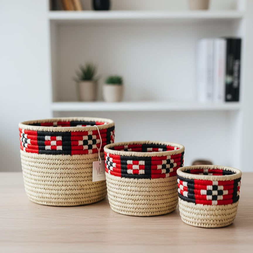 Three woven baskets with geometric patterns on a wooden surface, with a blurred background of books and plants.